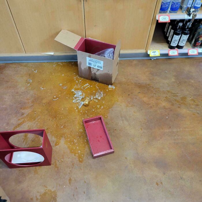 Broken glass and spilled liquid on store floor with packaging, illustrating unfortunate events in everyday life.