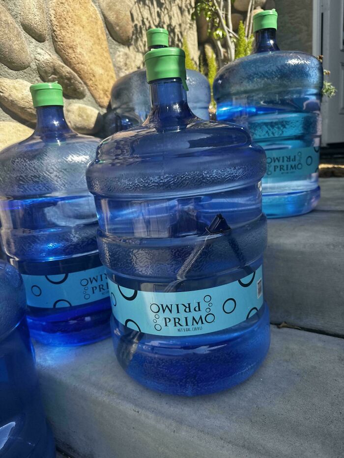 Large water jugs with green caps on concrete steps, showing an unfortunate event with a broken spout inside one jug.