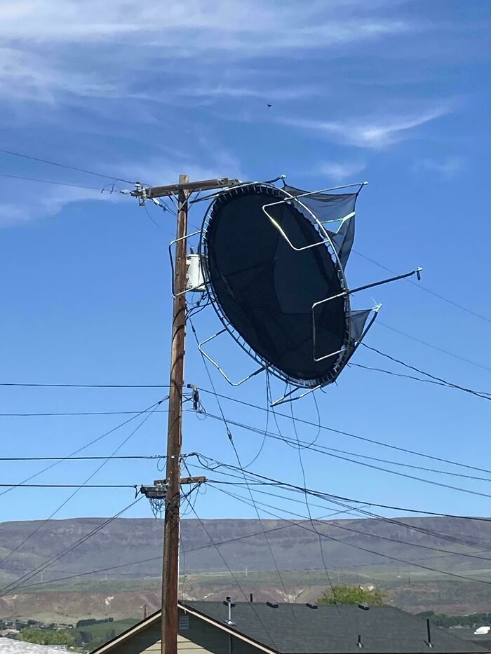 Trampoline caught and tangled on power lines and pole, an unfortunate event causing disruption and hazards outdoors.