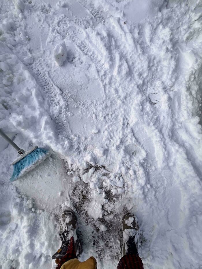 Snow-covered ground with a broom and footprints, showing an unfortunate event during snow cleanup.