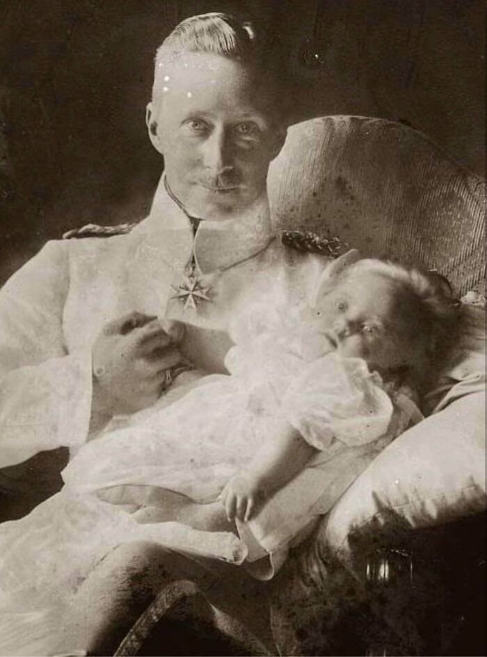 Black and white historical photograph of a man in uniform holding a baby, depicting a world you'd hardly recognize today.