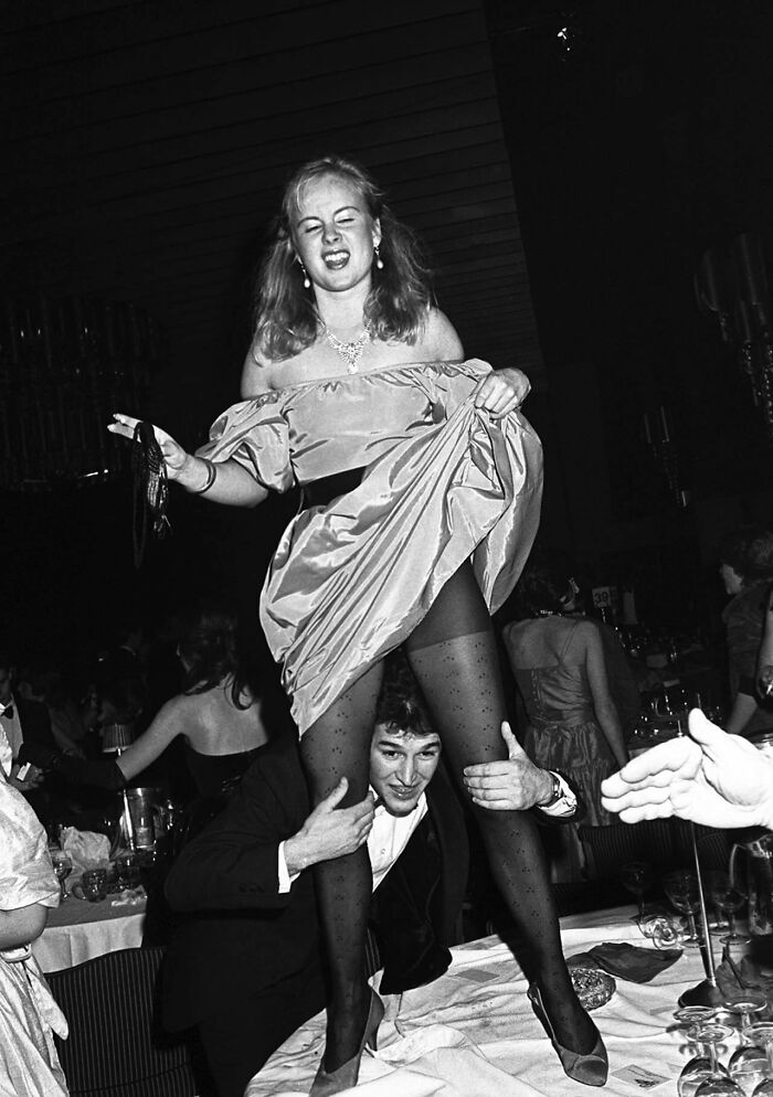 Vintage black and white photo showing lively party scene with a woman on a man's shoulders, depicting historical photographs.