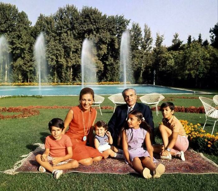Historical photograph of a family sitting on a rug in front of fountains and lush greenery, depicting a world hardly recognized today.