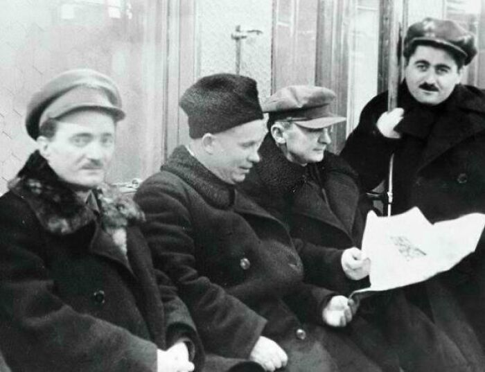 Four men in vintage coats and hats sitting together reading a newspaper in an interesting historical photograph.