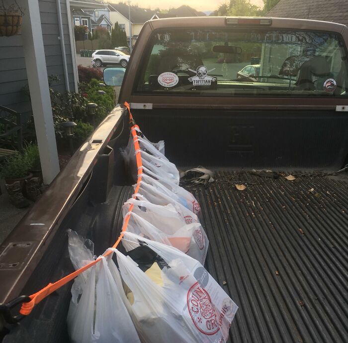 Plastic grocery bags secured with a strap along a truck bed edge, showing a clever but unconventional load method.