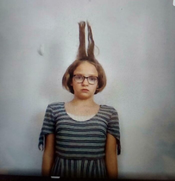 Young girl with glasses and striped dress with hair standing straight up, an unfortunate event caught on camera.