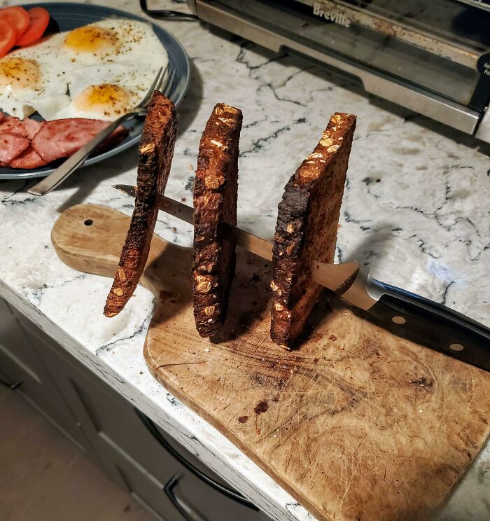 Knife stuck through three slices of burnt toast on a cutting board as a creative example of if it's stupid but it works then it's not stupid.