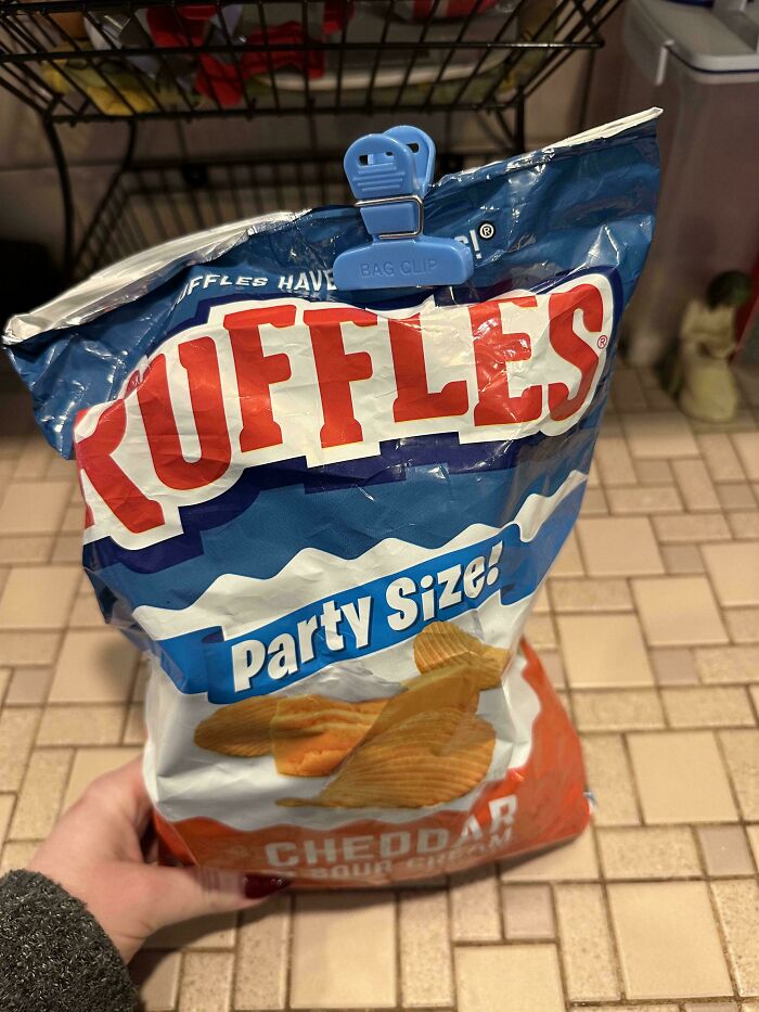 Partially opened party size Ruffles bag with cheddar sour cream chips held in kitchen, showing men being men example.