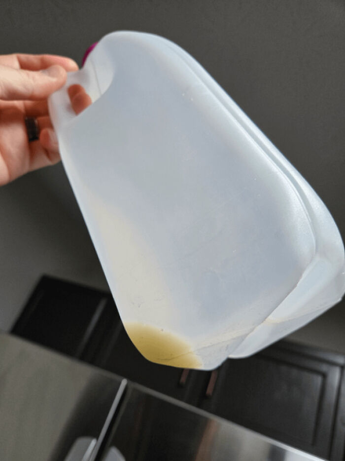 Hand holding nearly empty milk jug tilted with small amount of milk left, an example of men being men.