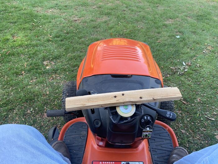 Riding lawn mower with a wooden plank attached to the controls, an example of if it’s stupid but it works.