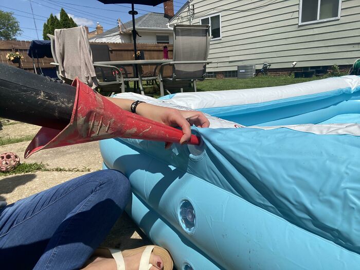 Using a red funnel to inflate a blue pool with a leaf blower in a backyard, example of clever hacks that work.