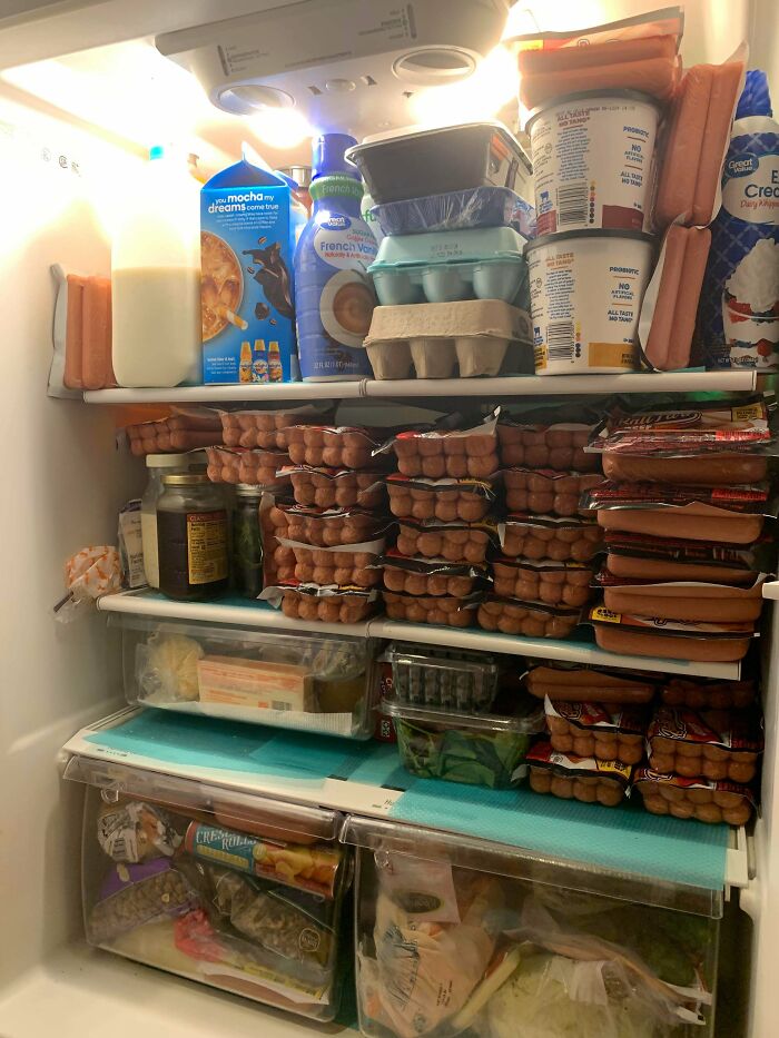 Fridge contents packed with multiple hot dog packs, eggs, dairy products, and snacks in an overstocked refrigerator.