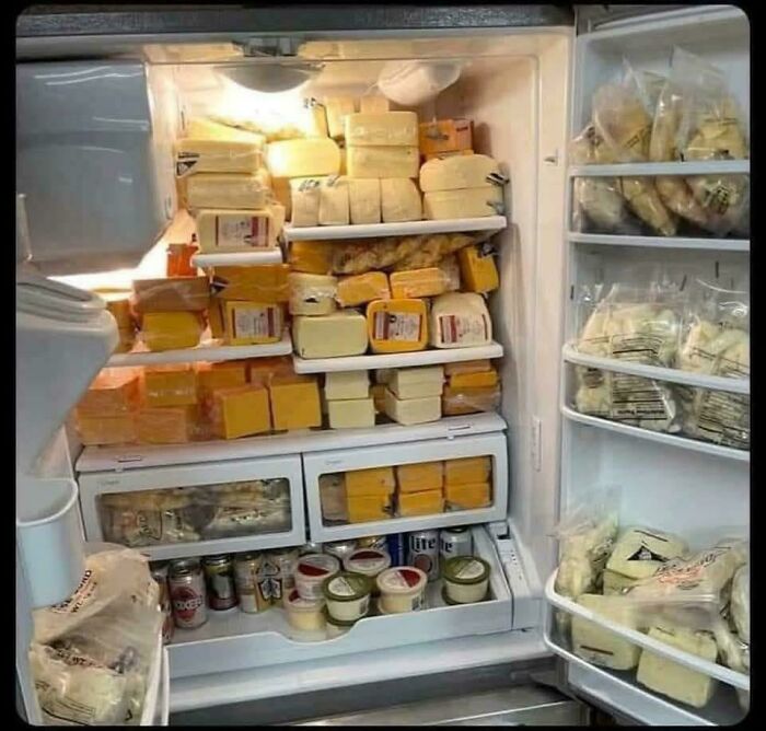 Open fridge packed with various cheeses, deli meats, and condiments showing interesting fridge contents lacking Pinterest aesthetic.
