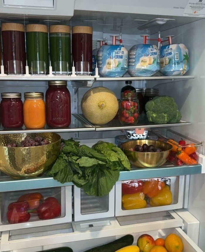 Fridge contents including fresh vegetables, fruits, juices, and packaged drinks in a neatly organized refrigerator.