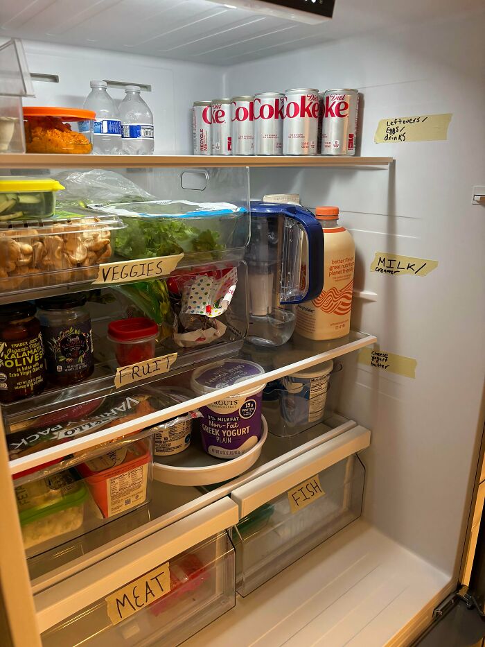 Organized fridge contents with labeled sections for veggies, fruit, meat, fish, and drinks, showing an interesting fridge setup.
