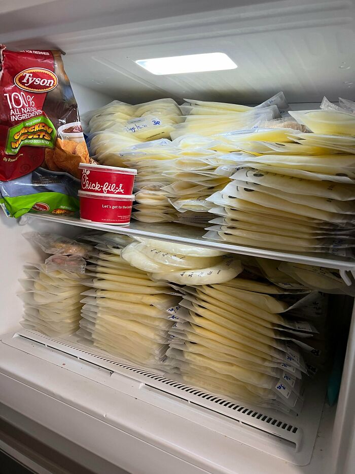 Fridge contents filled with numerous frozen breast milk bags stacked alongside frozen chicken nuggets and sauce cup.