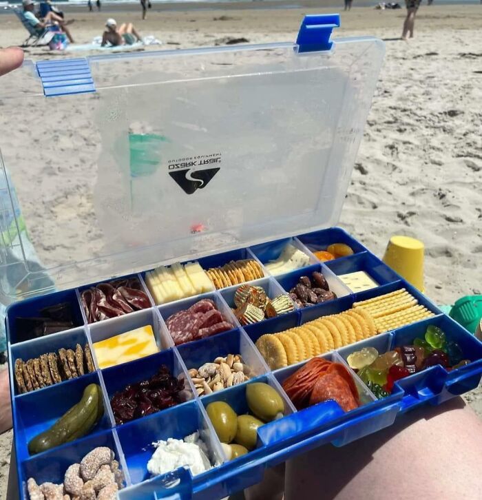 Snack box with crackers, cheese, olives, and meats on a beach, demonstrating clever food storage ideas that work well.