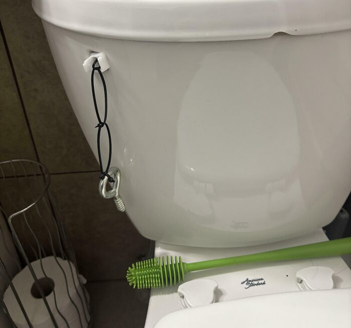 Toilet tank with a makeshift handle using elastic cords and a bolt as an example of if it's stupid but it works.