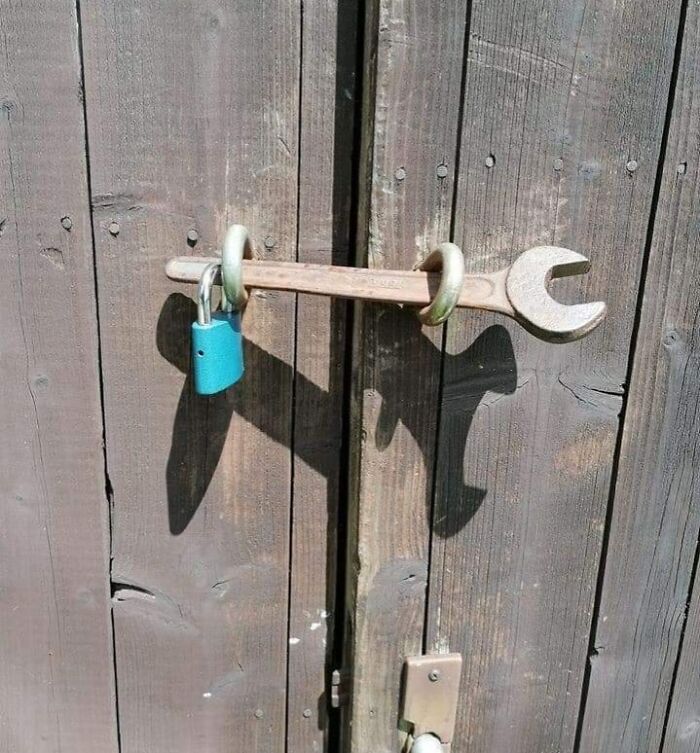 A creative example of a lock secured with a wrench and a padlock on a wooden door, showcasing if it's stupid but it works.