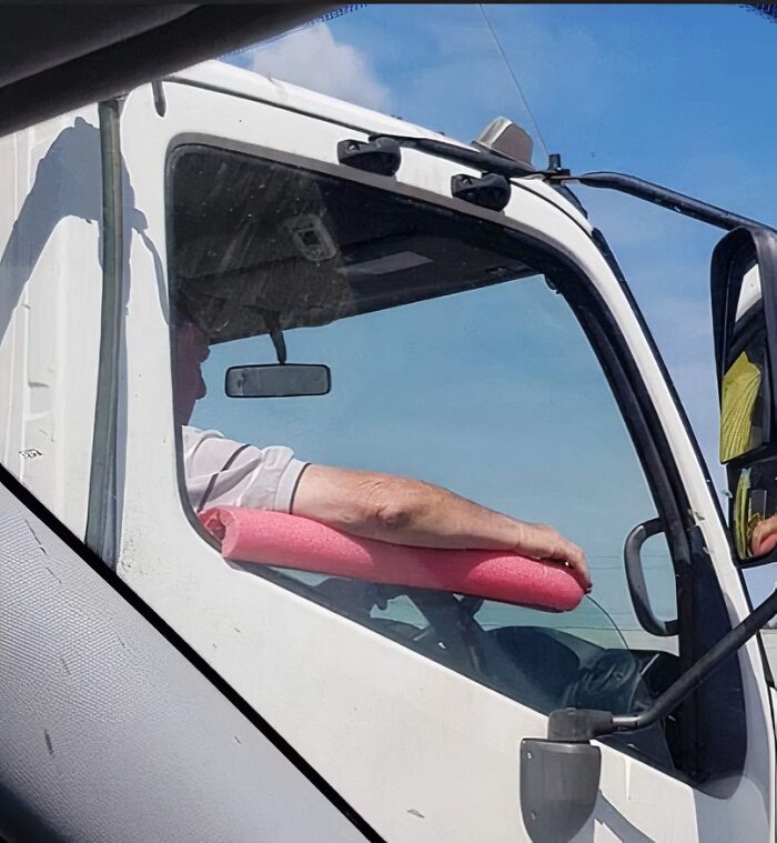Man resting his arm on a pink pool noodle as an improvised armrest inside a white truck cabin.