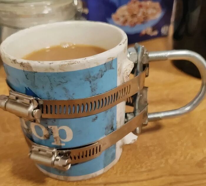 A broken coffee mug repaired with metal clamps and tape, demonstrating a clever if it works then it's not stupid fix.