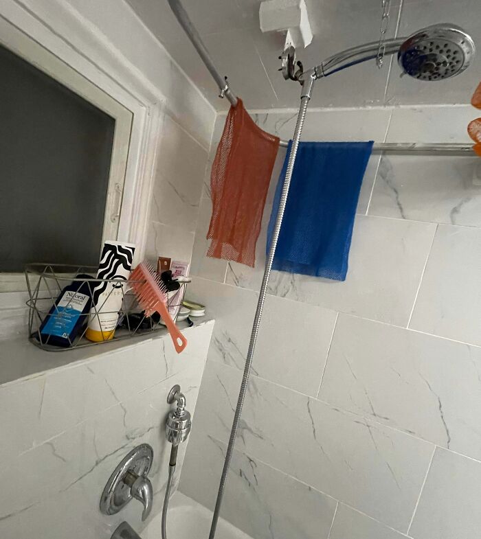 Shower fitted with a metal rod holding mesh bags and a hairbrush, an example of if it’s stupid but it works.