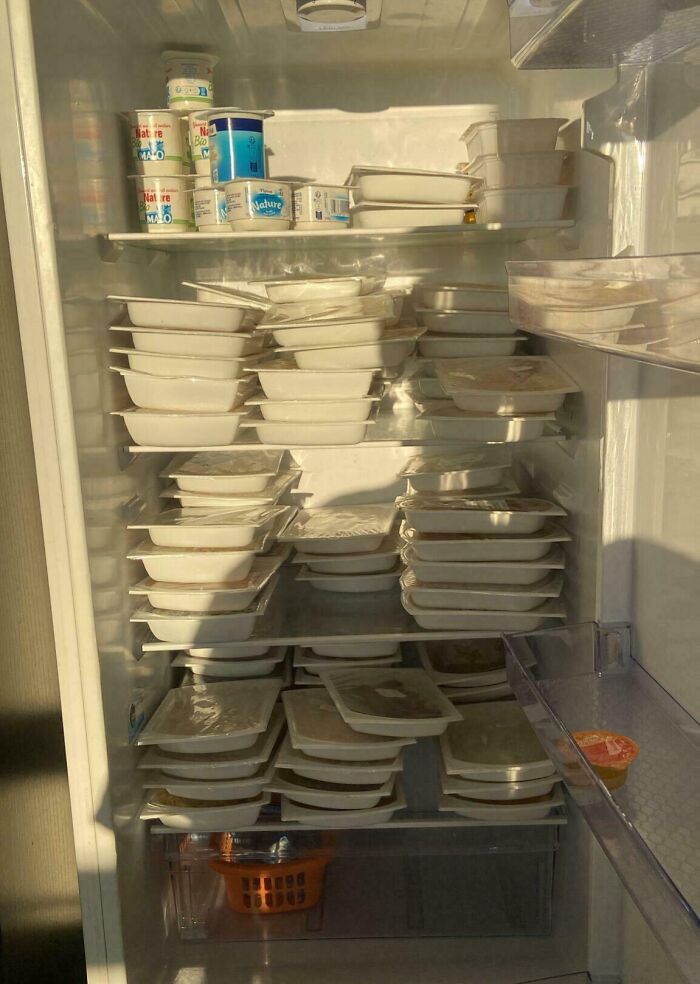 Overfilled fridge shelves stacked with numerous white plastic food containers and yogurt cups, showing unusual fridge contents.