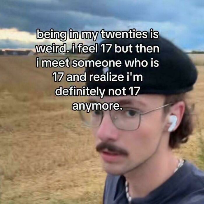 Young man with glasses and beret outdoors, relatable meme about feeling younger but realizing age difference, hilarious memes.