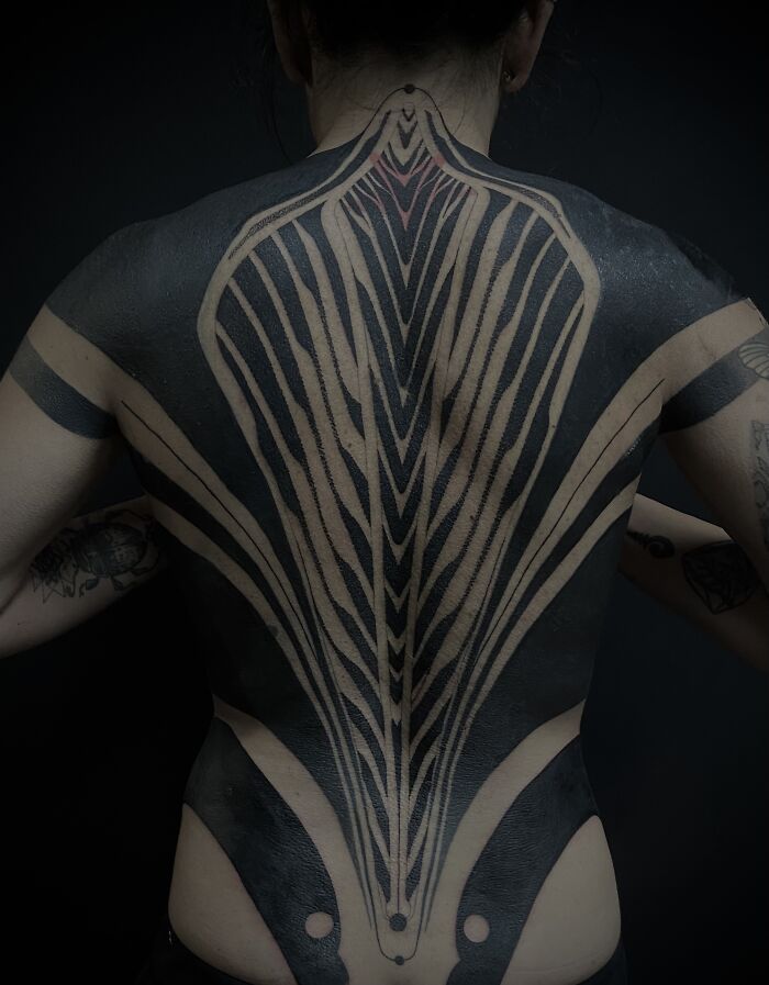 Large abstract black and beige tattoos cover a person’s back, showcasing cool tattoo designs with striking patterns and contrasts.