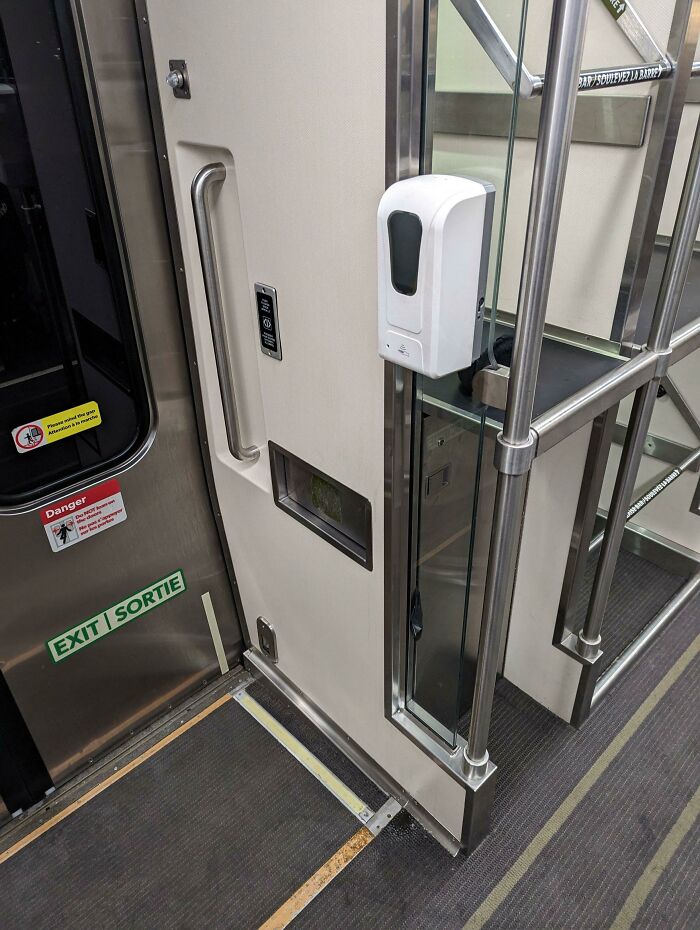 Confusing product design showing a hand sanitizer dispenser blocked by narrow space and metal bars on a train.