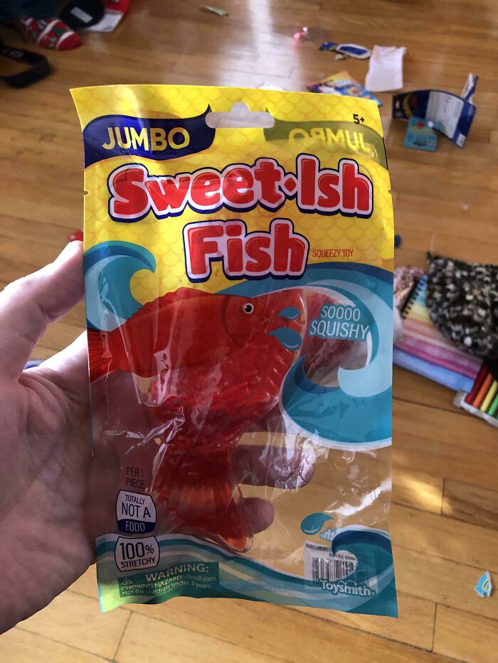Hand holding a jumbo sweet-ish fish toy packaging illustrating terrible product designs with confusing food-like appearance.