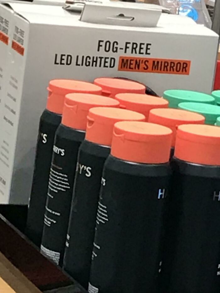 Bottles with bright orange caps labeled for men, next to a box advertising a fog-free LED lighted men's mirror.