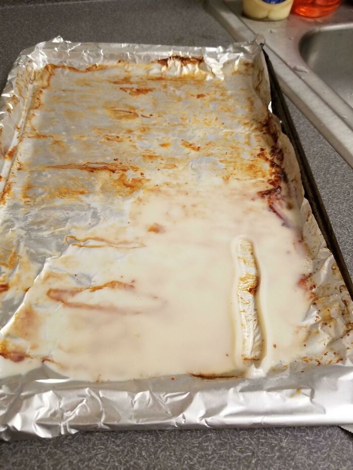 Baking tray lined with foil covered in spoiled milk residue, showcasing a roommate's messy kitchen behavior.