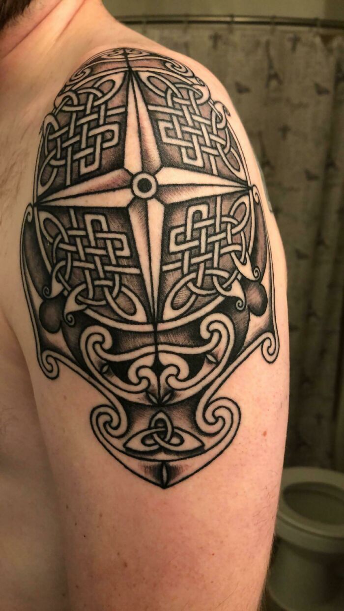 Black and grey Celtic compass tattoo with intricate knotwork design on a person's upper arm showcasing detailed line work.