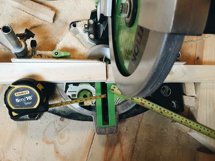 Compact miter saw cutting wood with misplaced measuring tape showing a DIY fail on a wooden workbench surface.