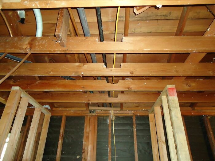 Exposed wooden ceiling beams with damaged wood and wiring showing a failed DIY construction project.