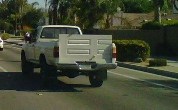 White pickup truck with a door awkwardly used as its tailgate, showcasing a major DIY fail on a city street.