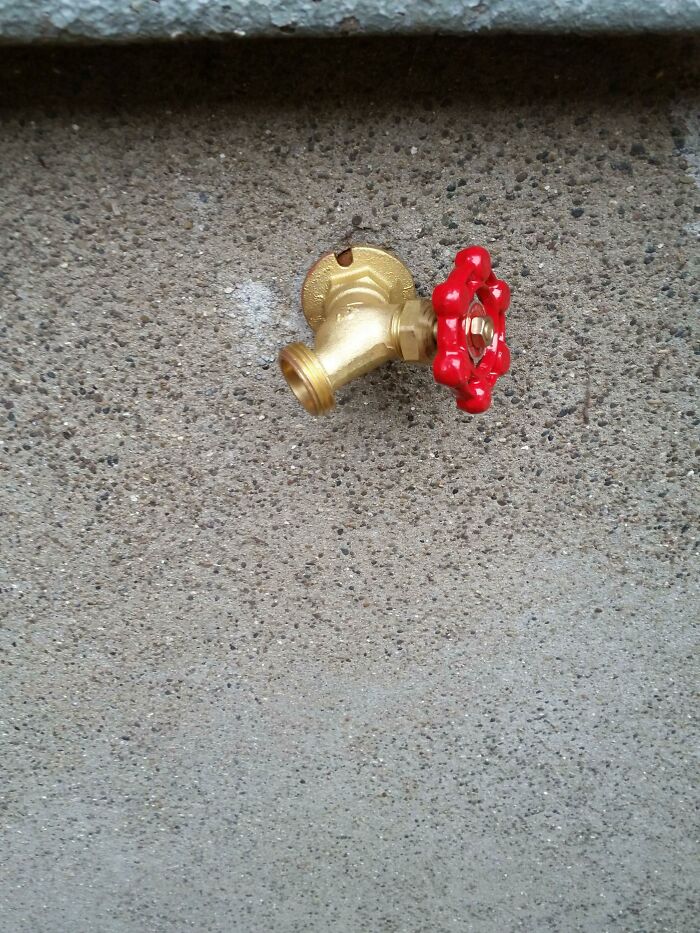 Gold outdoor faucet with a red handle installed incorrectly on a concrete wall showing a DIY fail example.