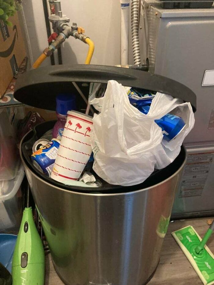 Overfilled trash can with plastic bag, paper cup, and cans, showing jerks that made roommates consider living alone.