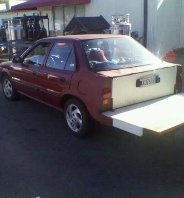 Red car with a poorly installed DIY wooden extension for the trunk, showcasing a failed DIY project on a street.