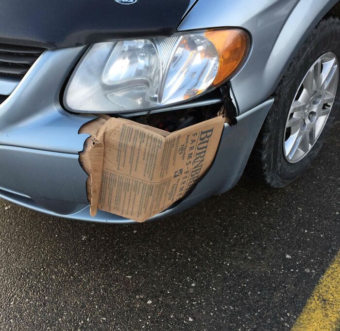 Car bumper damaged and temporarily patched with a cardboard piece illustrating a failed DIY repair attempt.