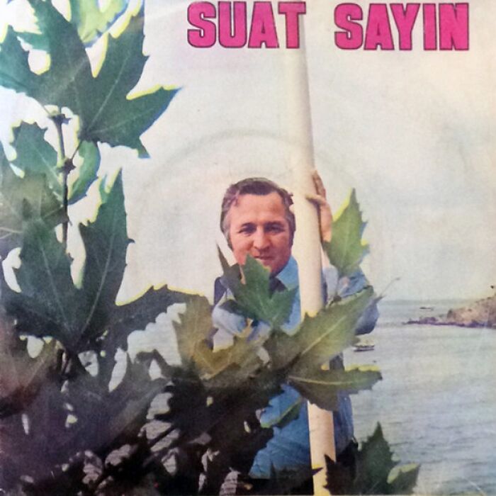 Man holding a pole among large leaves on a waterfront, featured on a hilariously bad album cover.