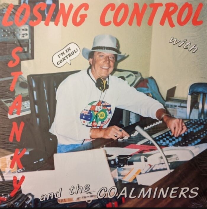 Man in white hat and colorful shirt smiling while mixing on soundboard, featured on hilariously bad album cover.