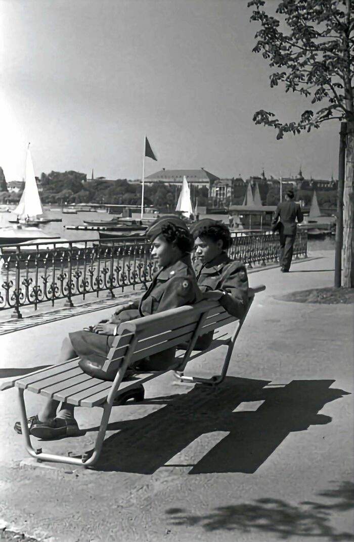 Two women in military uniforms relax on a bench by the waterfront in an interesting historical photograph.