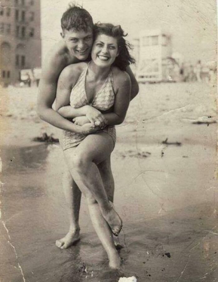 Couple smiling and posing playfully on a beach in an old historical photograph depicting a world you'd hardly recognize today.