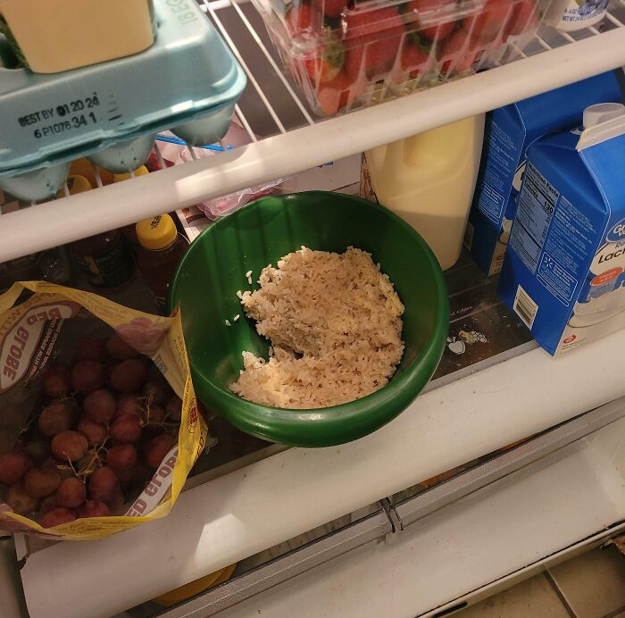 Leftover rice in a green bowl stored uncovered in a shared fridge, an example of jerks making roommates consider living alone.
