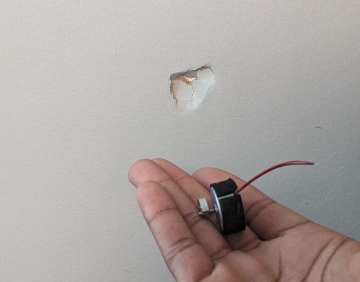 Hand holding a broken door lock part with a hole in the wall, showing jerks that made roommates consider living alone.