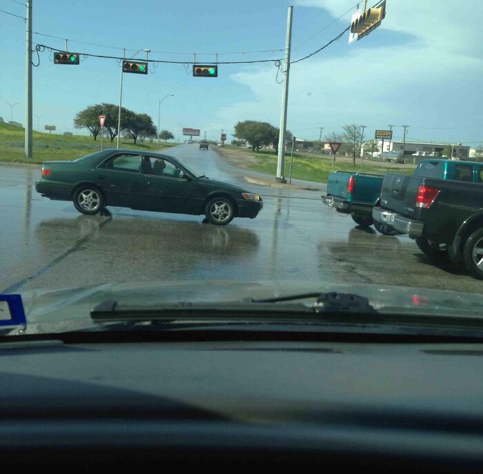 Car blocking intersection on wet road with traffic lights visible, illustrating dumb drivers causing dangerous situations.
