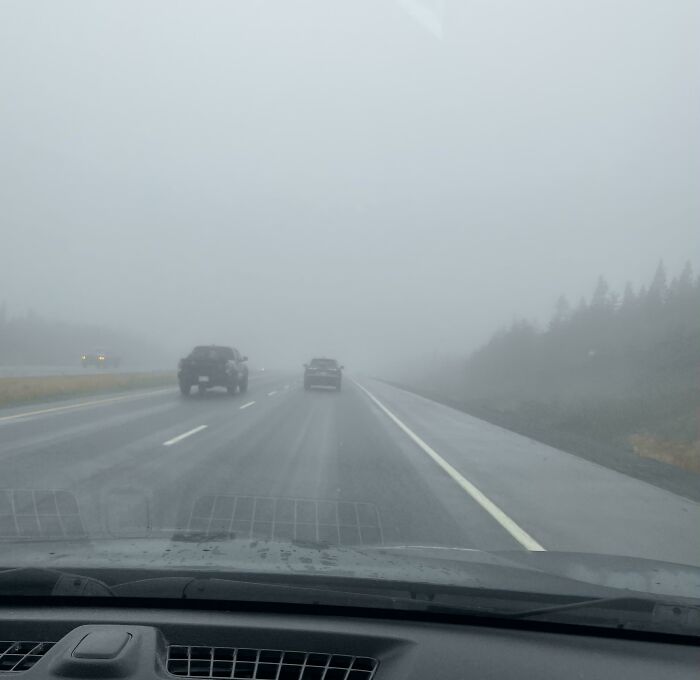 View from inside a car driving on a foggy highway with other vehicles, illustrating dangerous driving conditions.