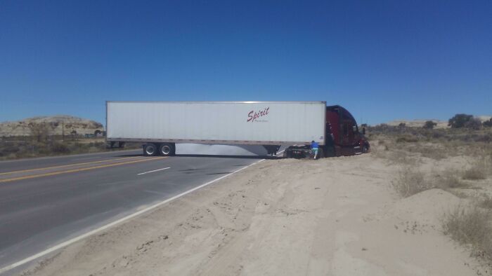 Semi-truck blocking the road with trailer stuck on the shoulder, an example of dumb drivers causing traffic issues.